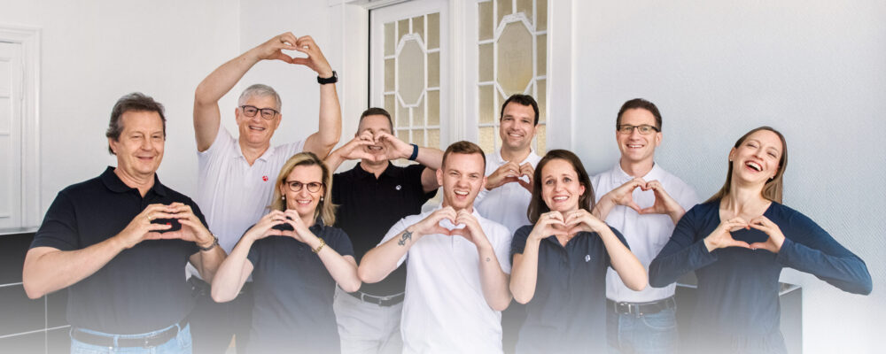 Teamfoto mit mehreren Mitarbeitern die ihre Hände jeweils zu einem Herz formen.